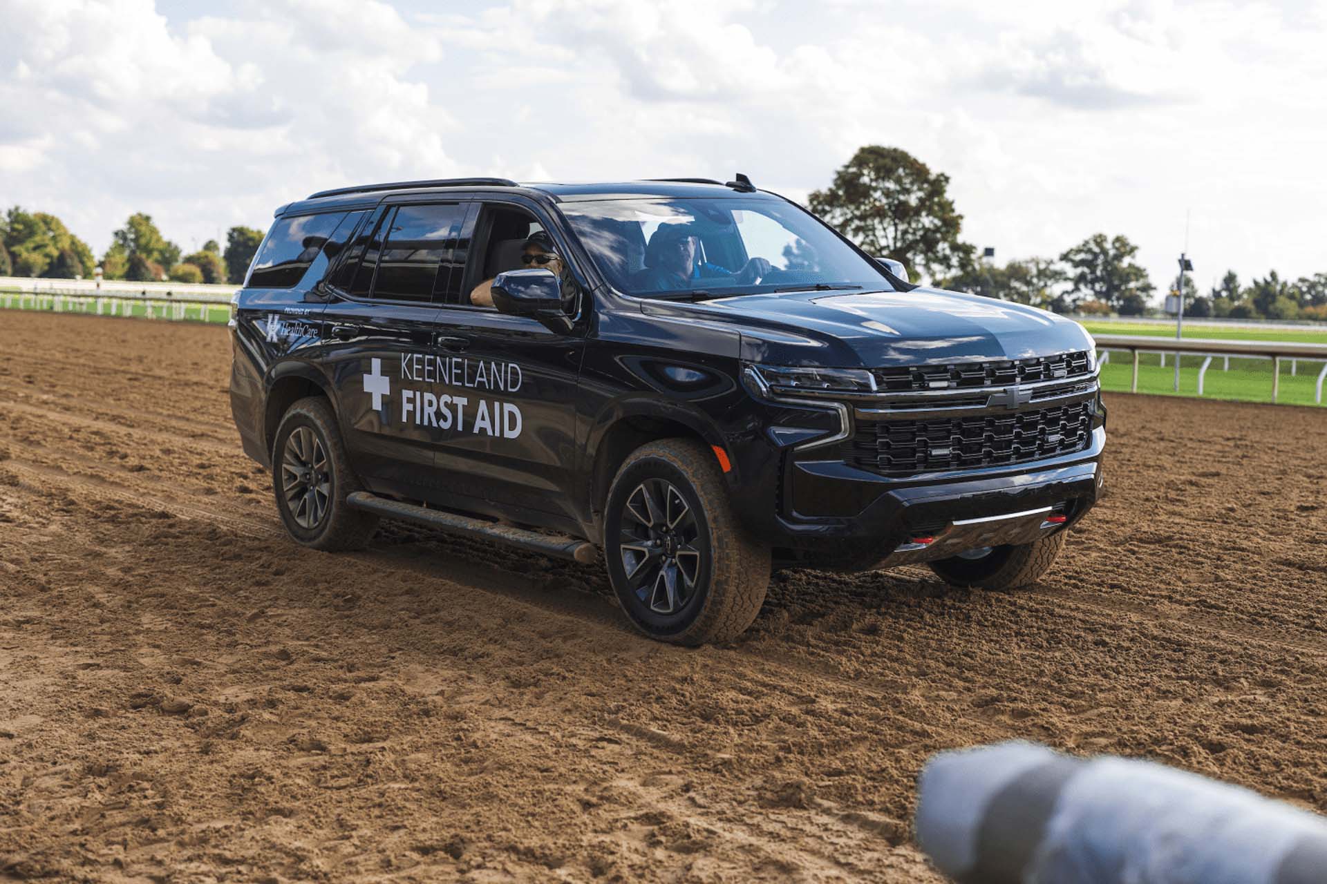 A picture of the Jockeytips First Aid car on the dirt track. It is a large black Chevy SUV.